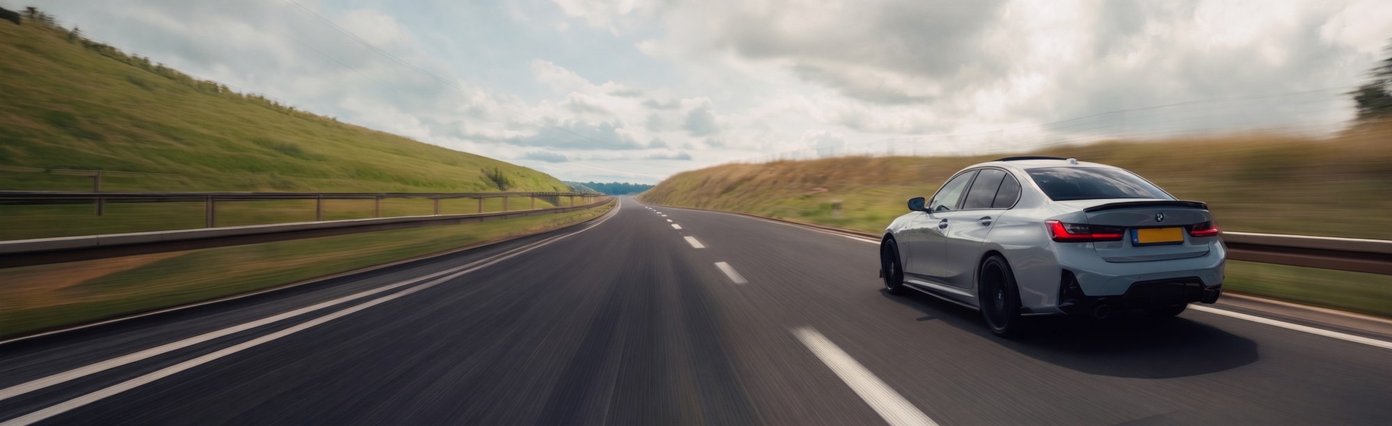 A silver saloon driving away on an open road, shot from behind at speed.